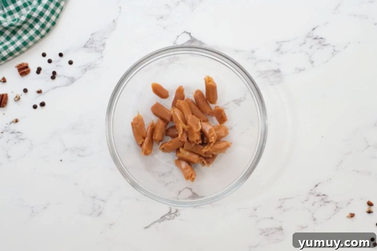 Irresistible Homemade Turtle Clusters 12 Unwrapped soft caramels neatly arranged in a clear glass bowl, ready for microwave melting.