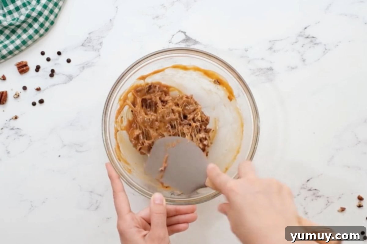 Irresistible Homemade Turtle Clusters 14 A rubber spatula gently folding together warm caramel and chopped pecans in a glass bowl.