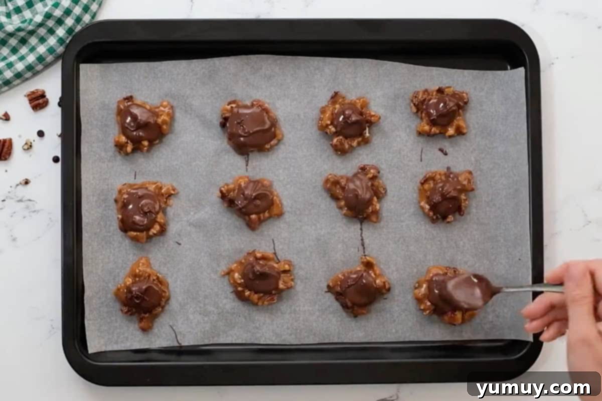 Irresistible Homemade Turtle Clusters 17 Melted chocolate being artfully spooned over pecan-caramel clusters arranged on a baking sheet, forming the top layer of the turtle candies.