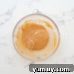 Irresistible Homemade Turtle Clusters 6 Melted caramel with coconut oil being stirred in a glass bowl.