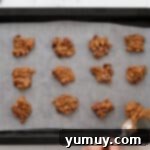 Irresistible Homemade Turtle Clusters 8 Small dollops of pecan-caramel mixture are being placed onto a lined baking sheet using two spoons, forming the base of the turtle candies.