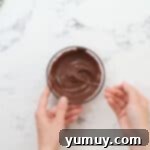 Irresistible Homemade Turtle Clusters 9 Melted chocolate is being stirred with a spoon in a clear glass bowl, showcasing its smooth, glossy texture.