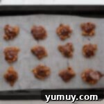Irresistible Homemade Turtle Clusters 10 Melted chocolate is being carefully spooned over individual pecan-caramel turtles on a baking sheet, creating their top layer.