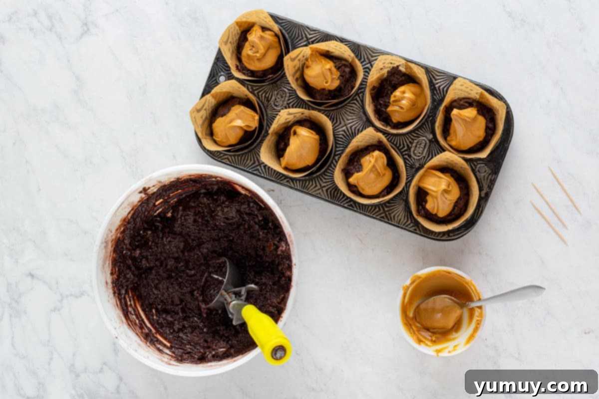 peanut butter spooned onto chocolate muffin batter in a muffin tin