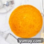 A perfectly baked pumpkin cheesecake, golden brown and smooth, resting on a white cake stand, ready to be served.