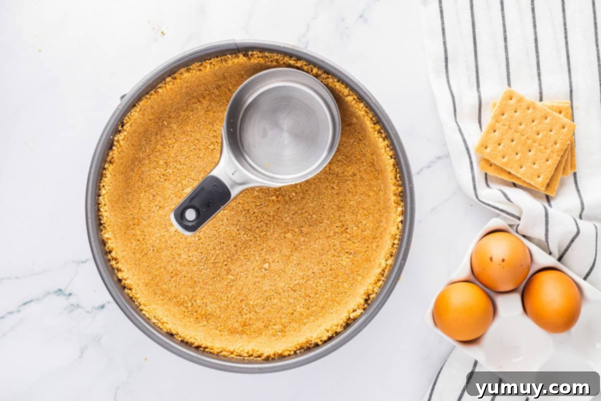 The process of pressing graham cracker crust mixture into the base and sides of a springform pan using a glass for an even layer.