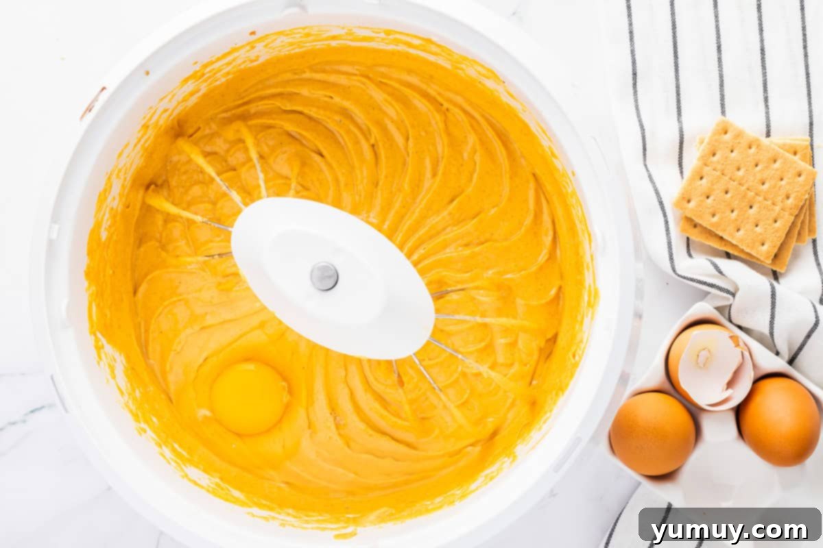 Whole eggs being carefully added, one by one, to the vibrant orange cheesecake filling in a mixing bowl.