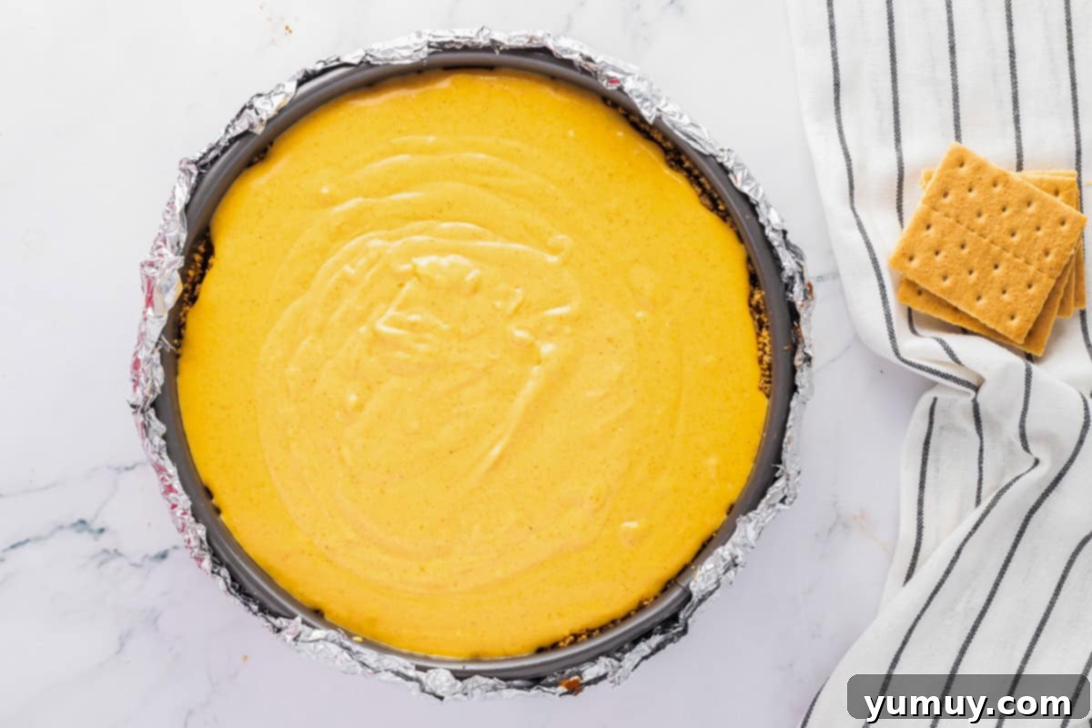 The smooth, unbaked pumpkin cheesecake batter filling a foil-wrapped springform pan, resting on a baking sheet.