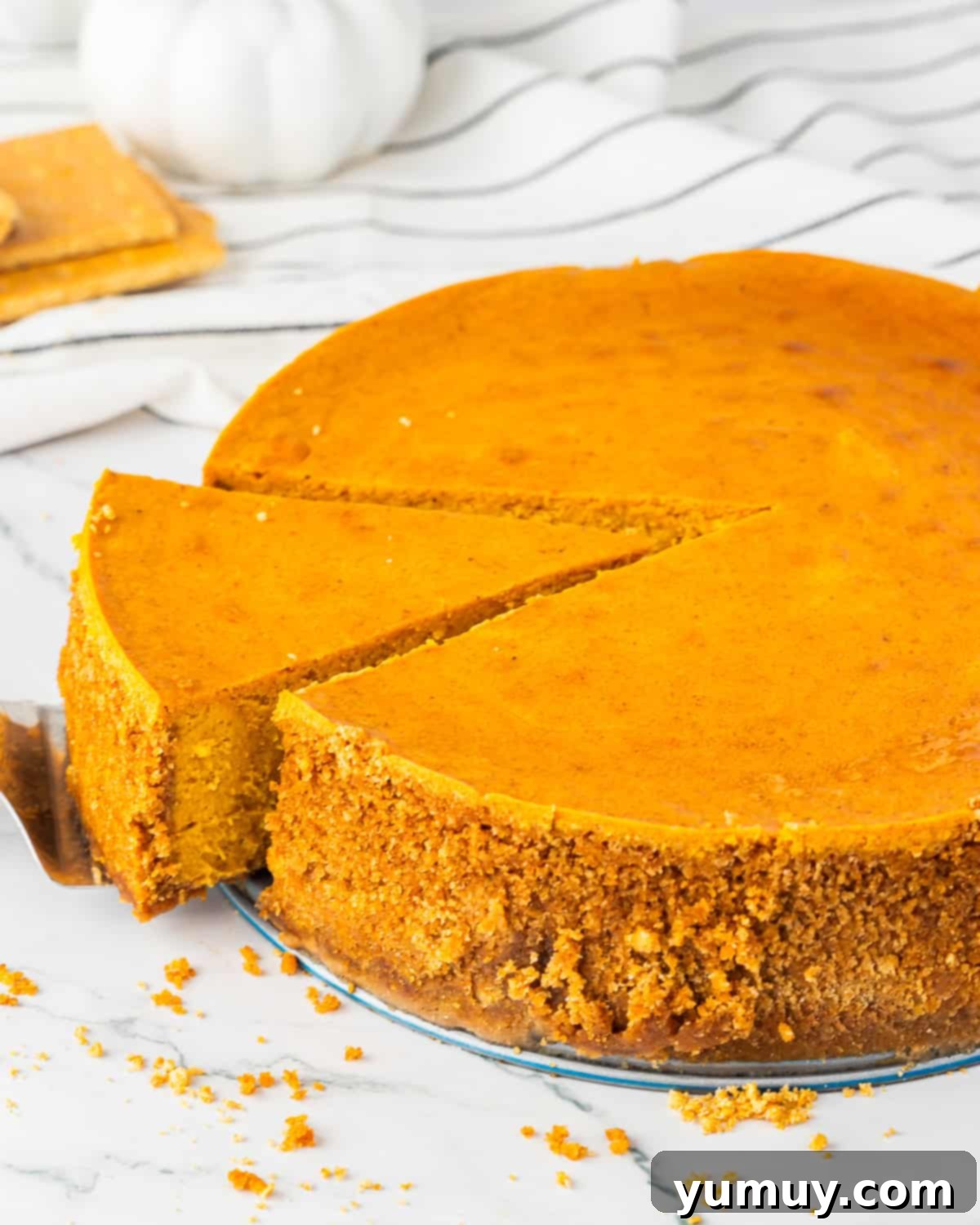 A cake server elegantly lifting a pristine slice of pumpkin cheesecake from a whole cake, showcasing its smooth texture and perfect layers.