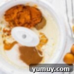 Rich orange pumpkin puree being added to a bowl of creamy, beaten cream cheese, ready to be mixed into the cheesecake filling.