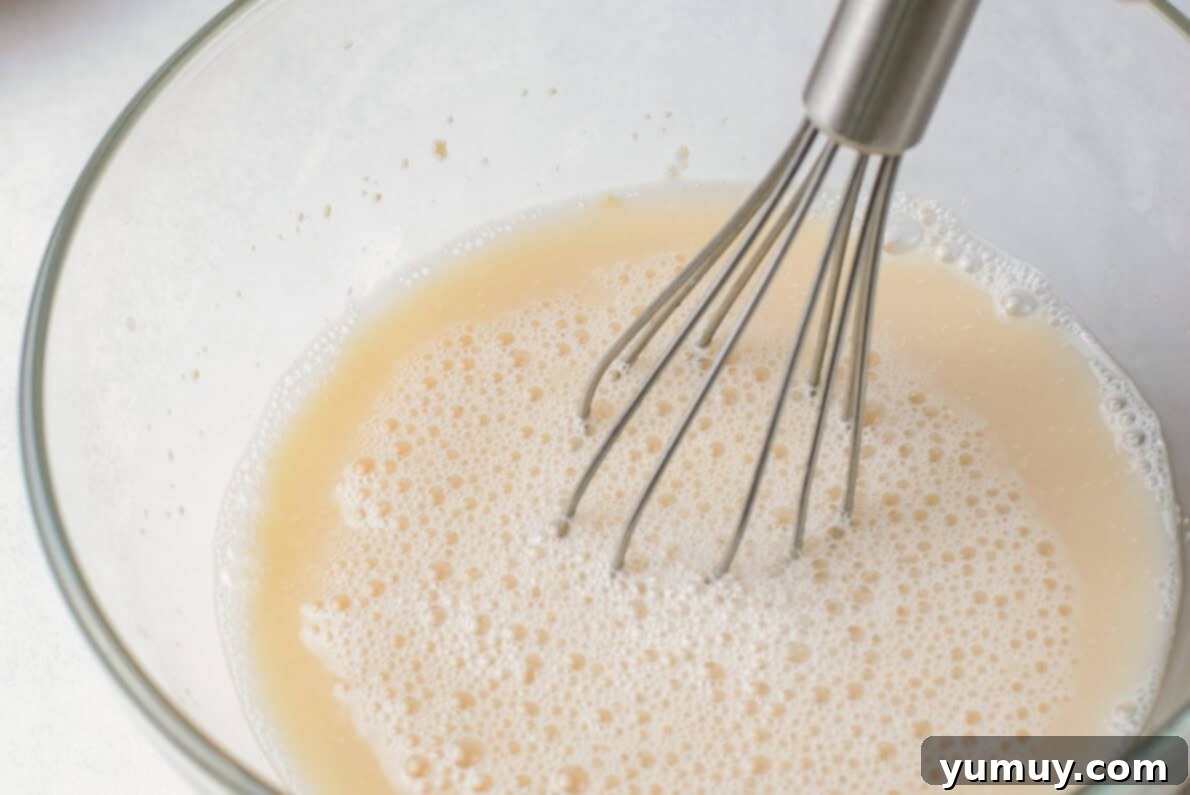 Homemade Krispy Kreme Glazed Donuts 13 a person whisking a liquid into a glass bowl.