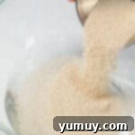 Homemade Krispy Kreme Glazed Donuts 5 a person pouring sugar into a glass bowl.