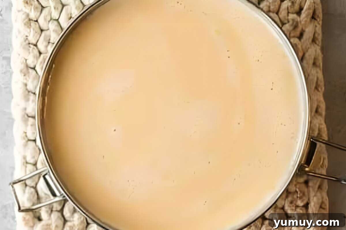 The smooth custard mixture being poured into a round pan, through a sieve, on top of the cooled caramel.