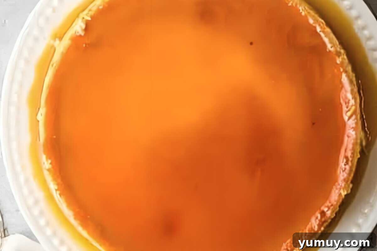 A beautifully unmolded flan, drenched in its glossy caramel sauce, presented on a white serving dish.