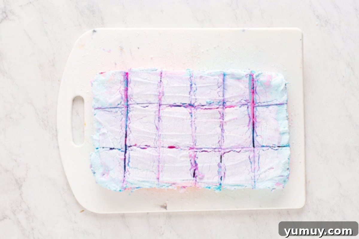 Spun Sugar Pillows 16 Neatly cut 1-inch squares of set cotton candy marshmallows, displaying their vibrant pink and blue colors, arranged on a white cutting board.