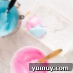 Spun Sugar Pillows 8 Pink and blue marshmallow mixtures being carefully added to a white rectangular baking pan in alternating layers.