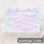 Spun Sugar Pillows 9 Swirled cotton candy marshmallow mixture, showing vibrant pink and blue colors, settling in a white rectangular pan.