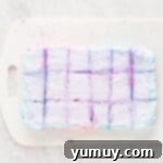 Spun Sugar Pillows 10 A grid of perfectly set cotton candy marshmallows, cut into 1-inch squares, on a white cutting board.