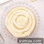 Buttercream frosting expertly piped in a beautiful spiral onto a layer of easy homemade wedding cake, resting on a glass cake stand.