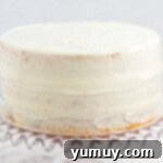 A perfectly crumb-coated easy homemade wedding cake, resting on a glass cake stand, ready for its final decorative layer of frosting.