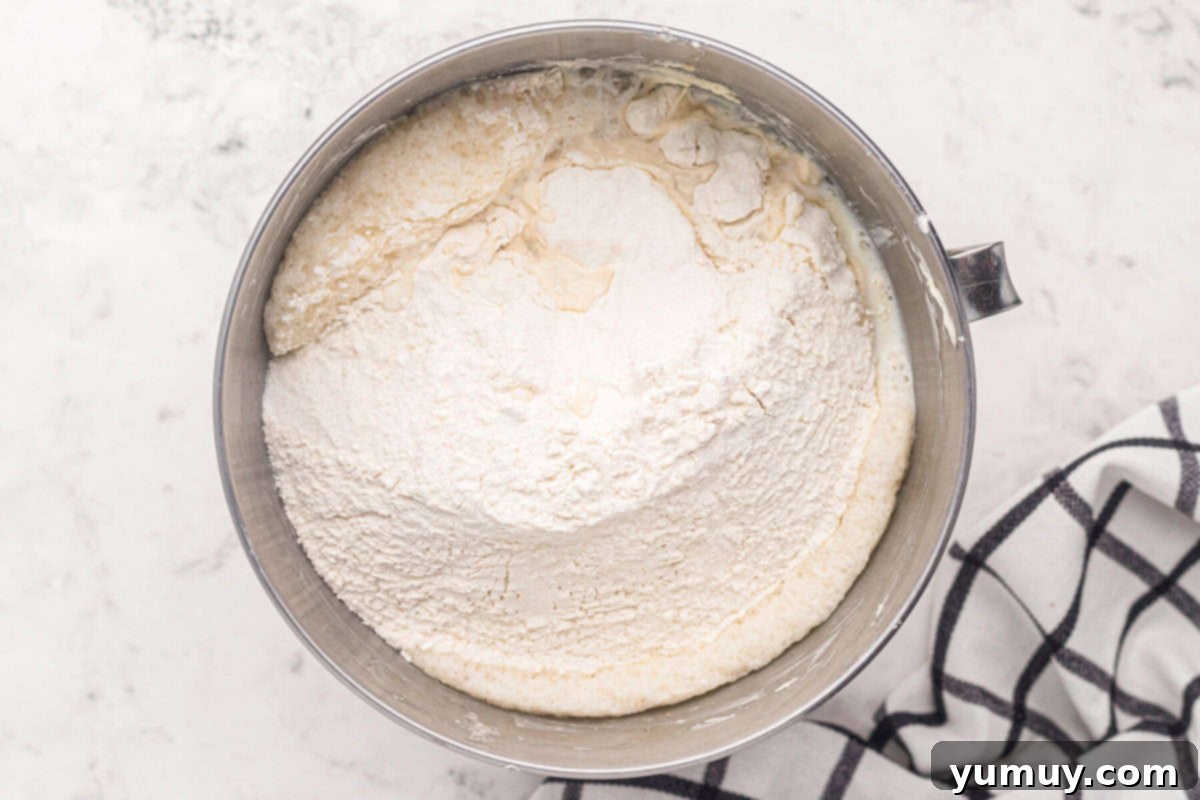 Dry ingredients for easy homemade wedding cake being carefully added to the wet mixture in a stainless steel mixing bowl, ensuring thorough blending.