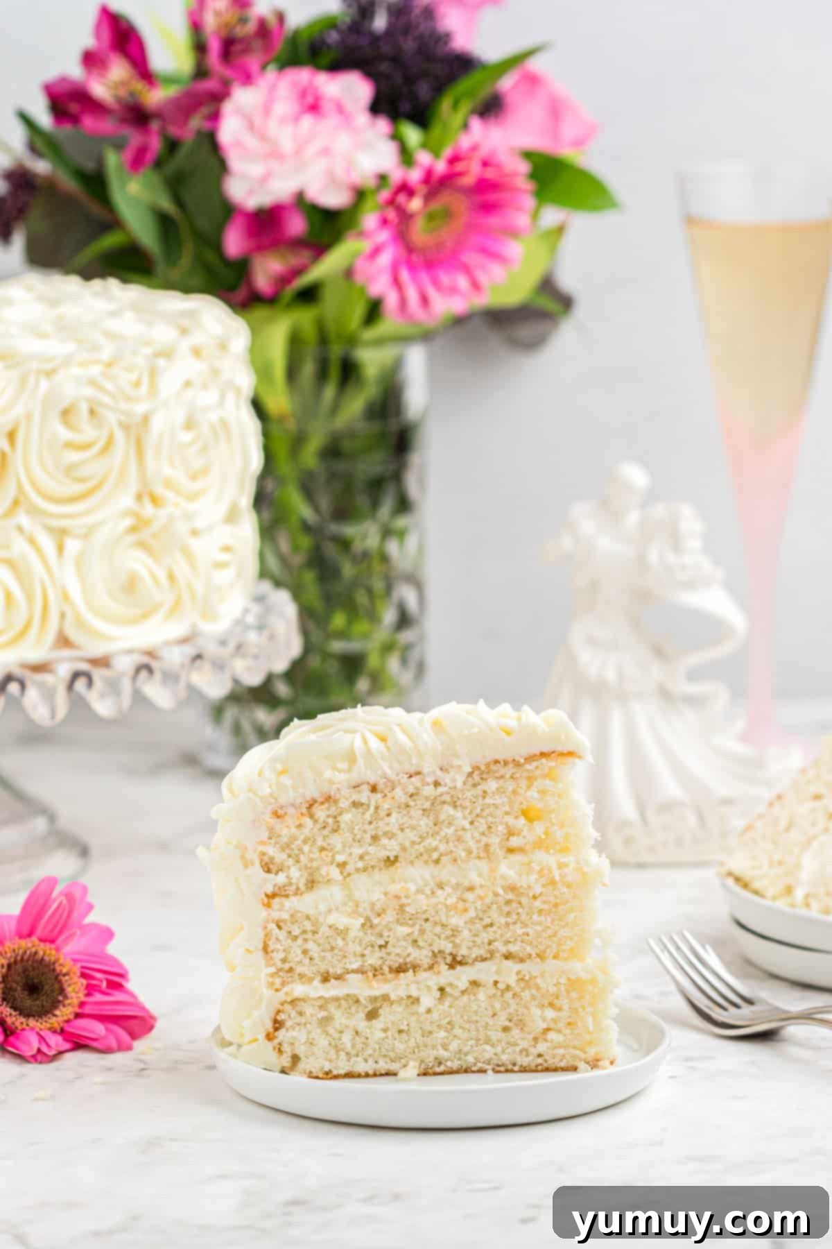 A perfectly sliced piece of homemade white wedding cake, revealing its moist layers and creamy frosting, resting on a pristine white plate.