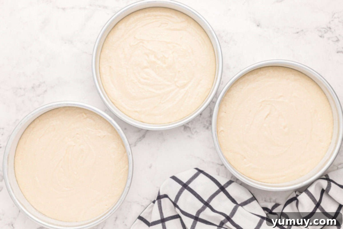 Easy homemade wedding cake batter perfectly divided among three round cake pans, ready for the oven and uniform baking.