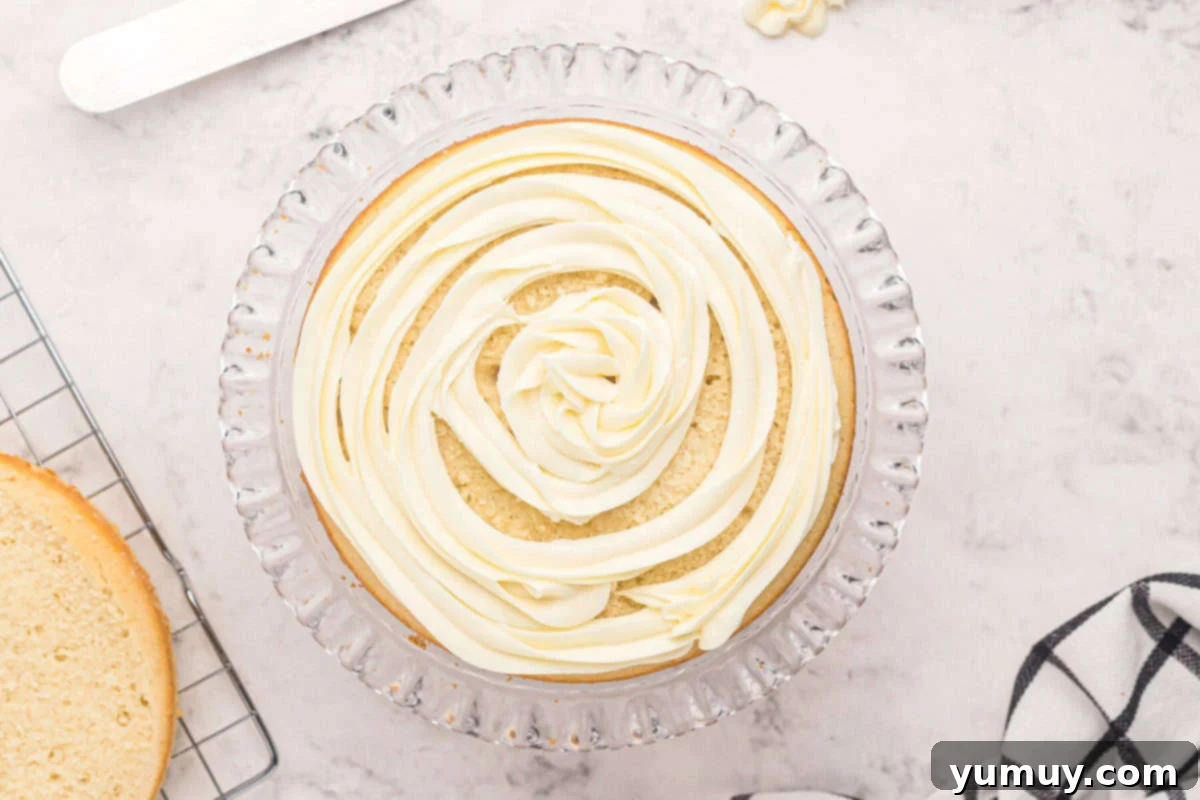 Buttercream frosting expertly piped in a beautiful spiral onto a layer of easy homemade wedding cake, resting on a glass cake stand, ready for the next layer.