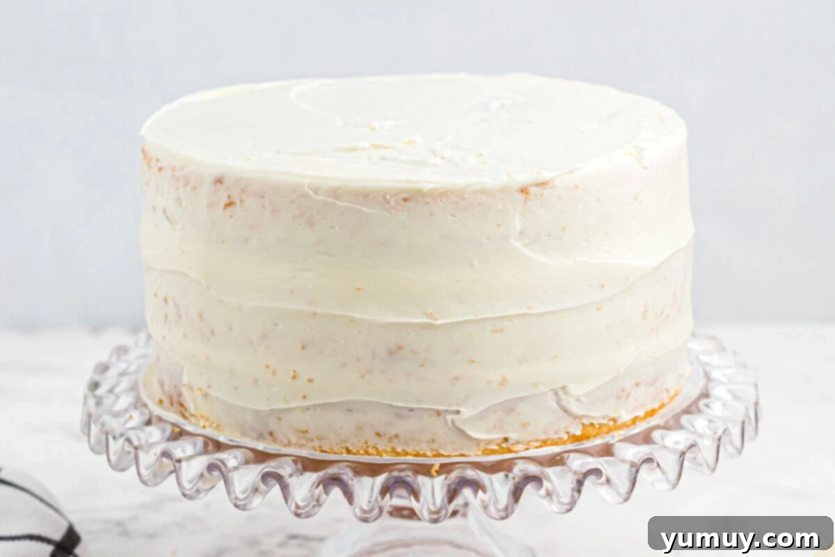 A perfectly crumb-coated easy homemade wedding cake, resting on a glass cake stand, showcasing a smooth base for final decoration.