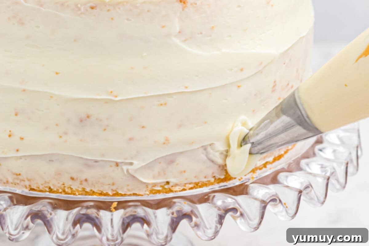 A close-up of piping delicate buttercream rosettes onto an easy homemade wedding cake, demonstrating the technique on a glass cake stand.
