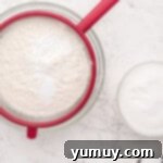 Dry ingredients for easy homemade wedding cake being carefully sifted into a clear glass bowl, ensuring a smooth batter.