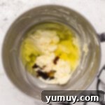 Eggs and vanilla are gently added to the wet ingredients for easy homemade wedding cake in a polished stainless steel mixing bowl.
