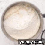 Dry ingredients for easy homemade wedding cake are progressively added to the wet mixture in a shining stainless steel mixing bowl.