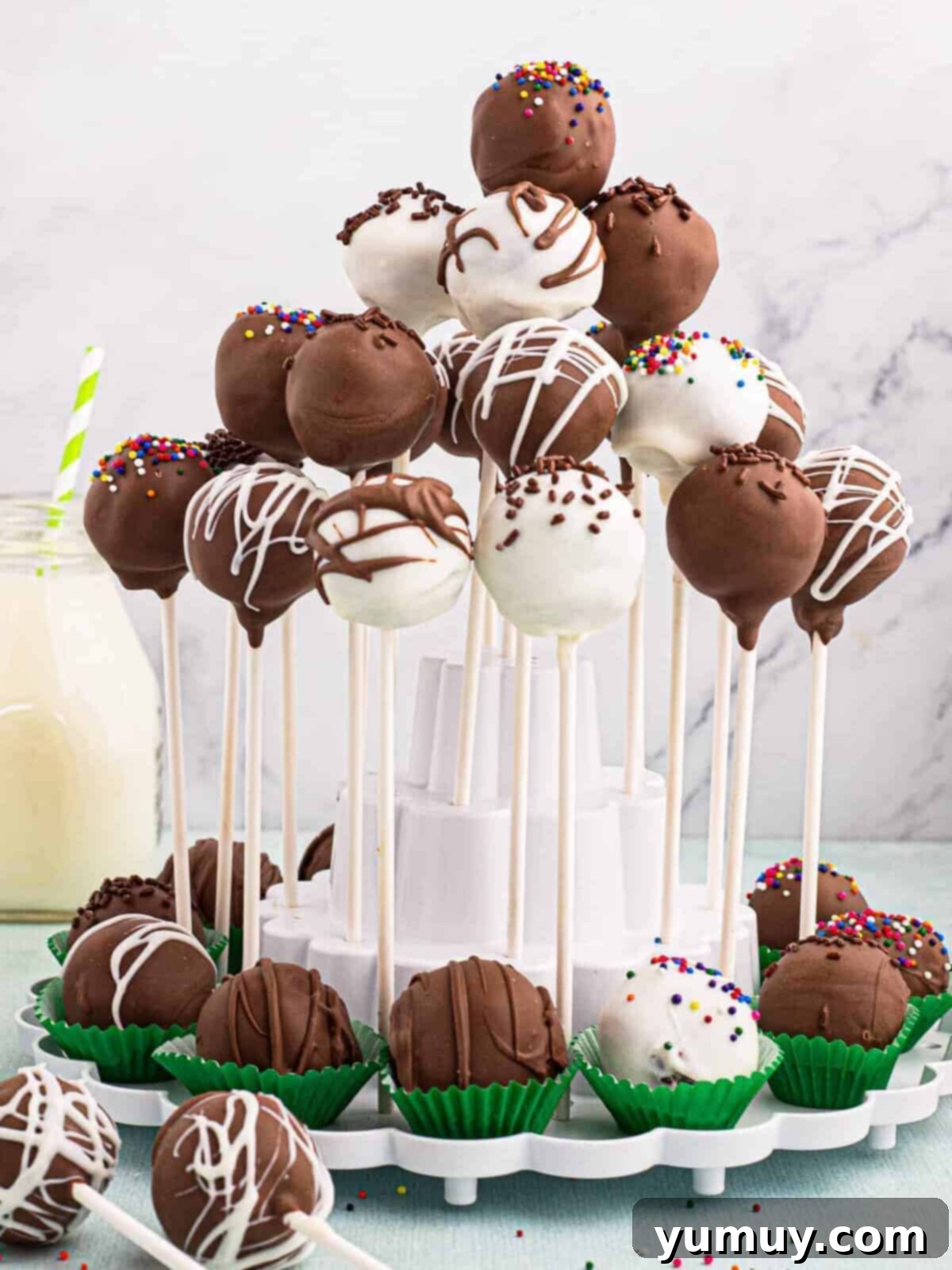 A display of perfectly round chocolate cake pops on a tiered stand, some decorated with sprinkles, ideal for a party.