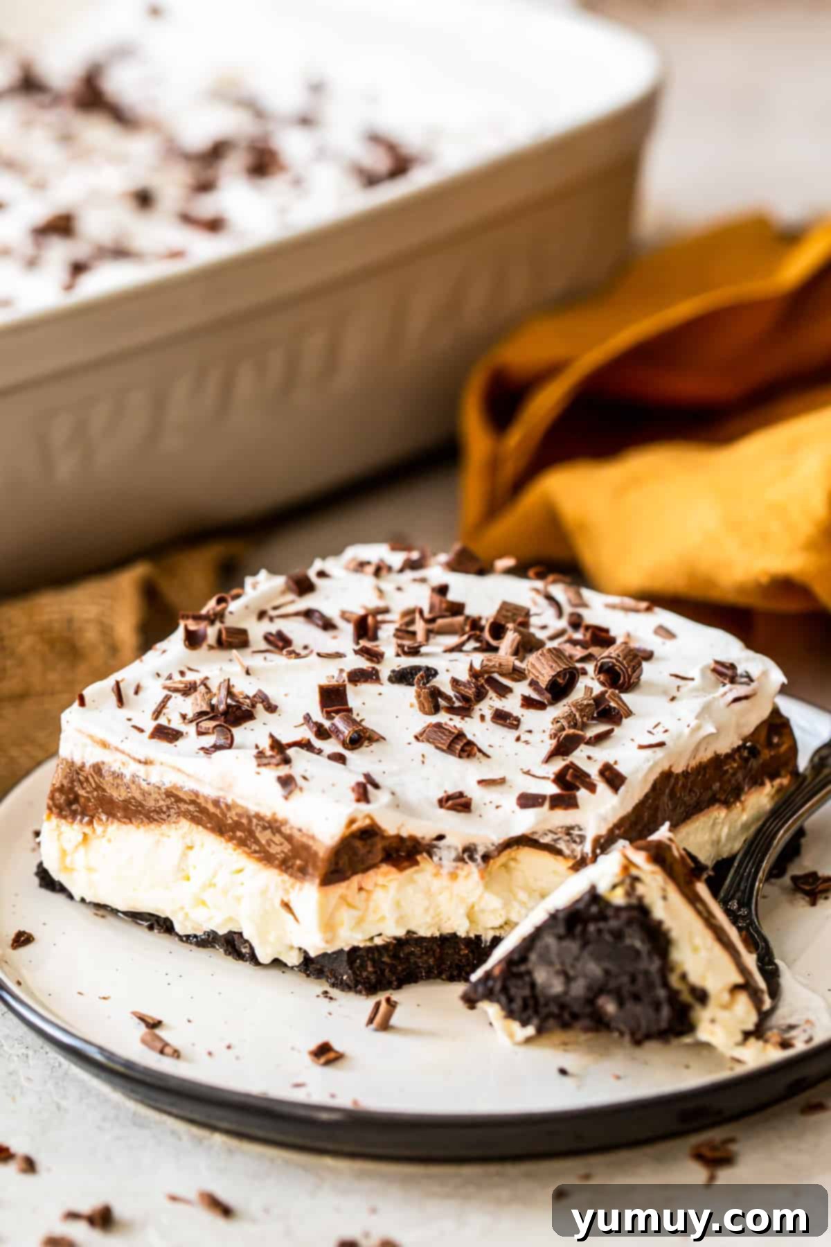 A perfectly portioned slice of no-bake chocolate lasagna, revealing layers of cookie crust, cream cheese, pudding, and whipped cream on a white plate.