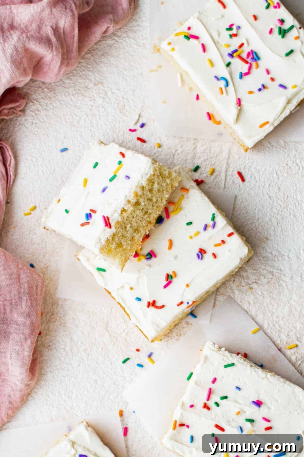 Stacked slices of light and fluffy vanilla sheet cake, generously frosted and adorned with colorful sprinkles, ready for a party.