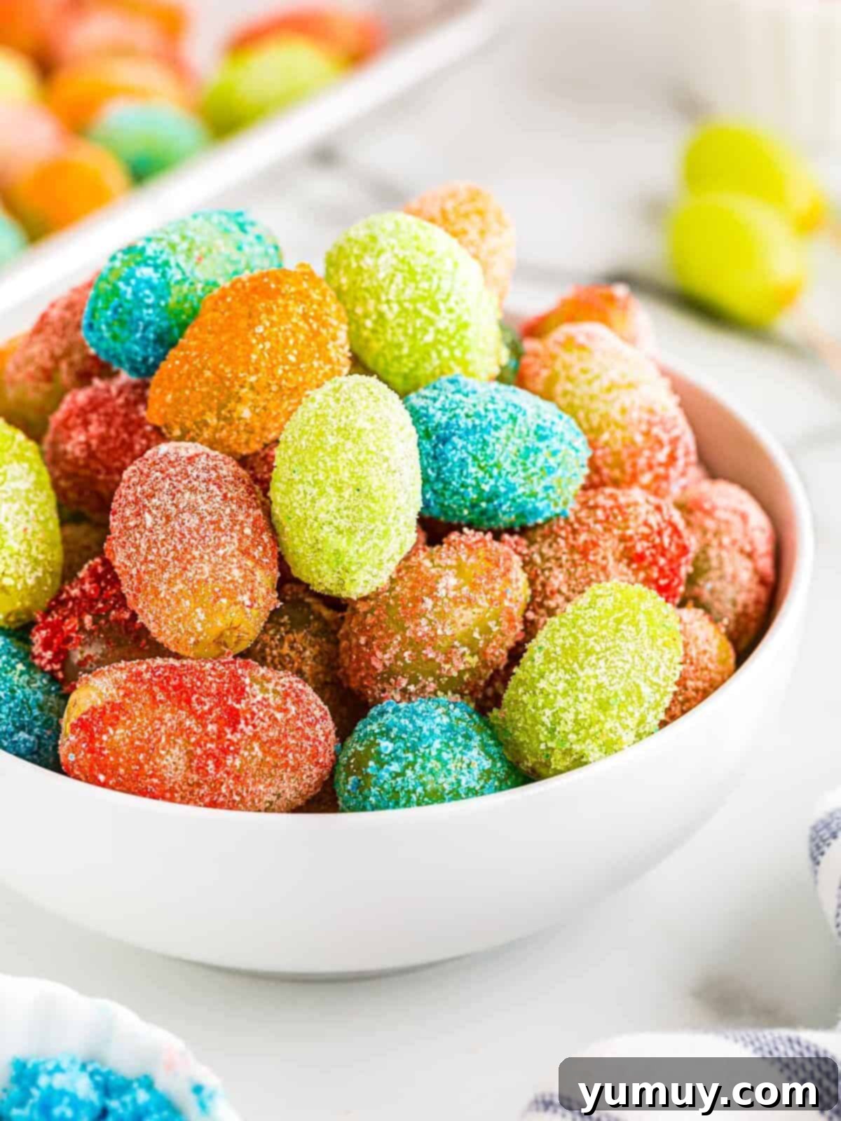 A vibrant bowl of colorful candy grapes, coated in Jello powder, offering a sweet and tangy snack option.