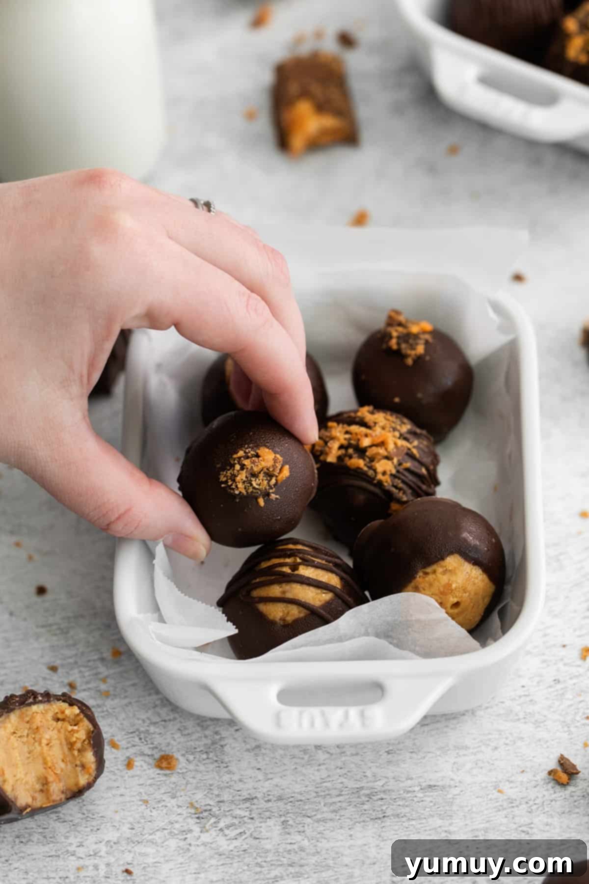 A hand reaching for one of six delightful Butterfinger balls, perfectly arranged in a white serving dish.