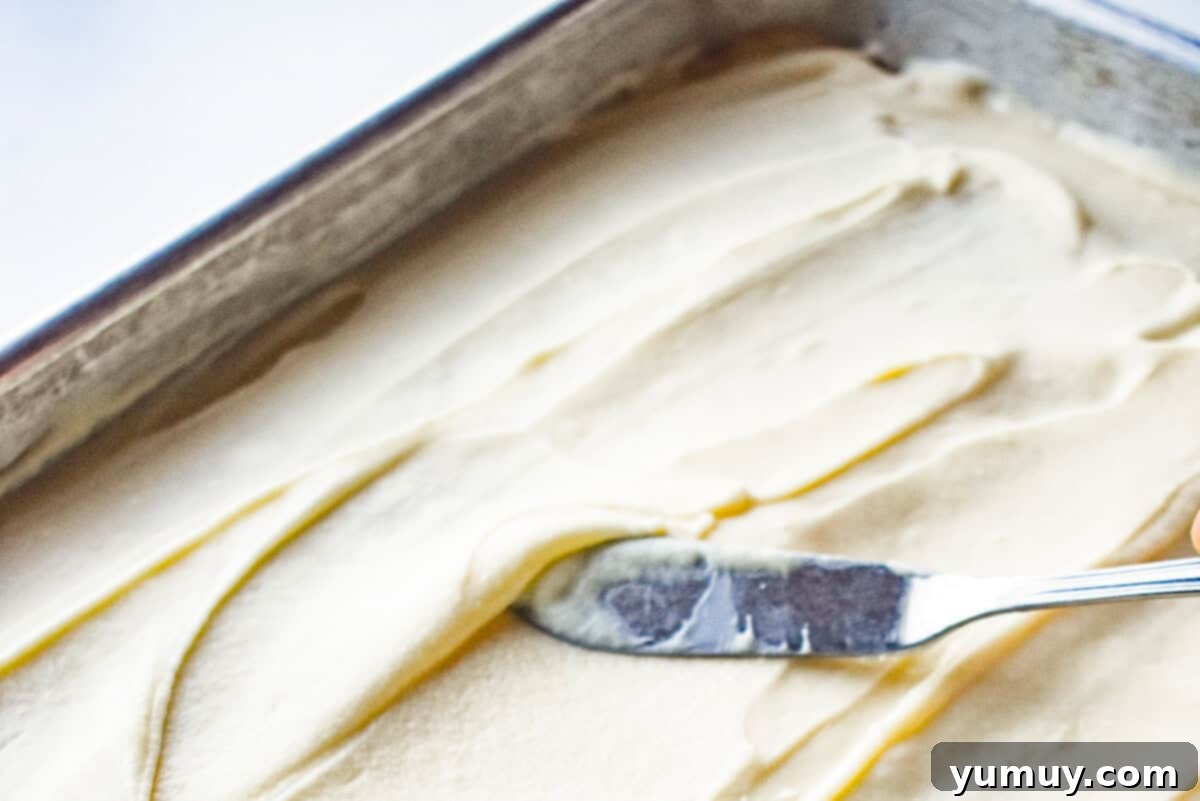 A freshly frosted eggnog sheet cake in a 9x13 inch pan, featuring a silky smooth top surface, with an offset spatula neatly placed beside it.