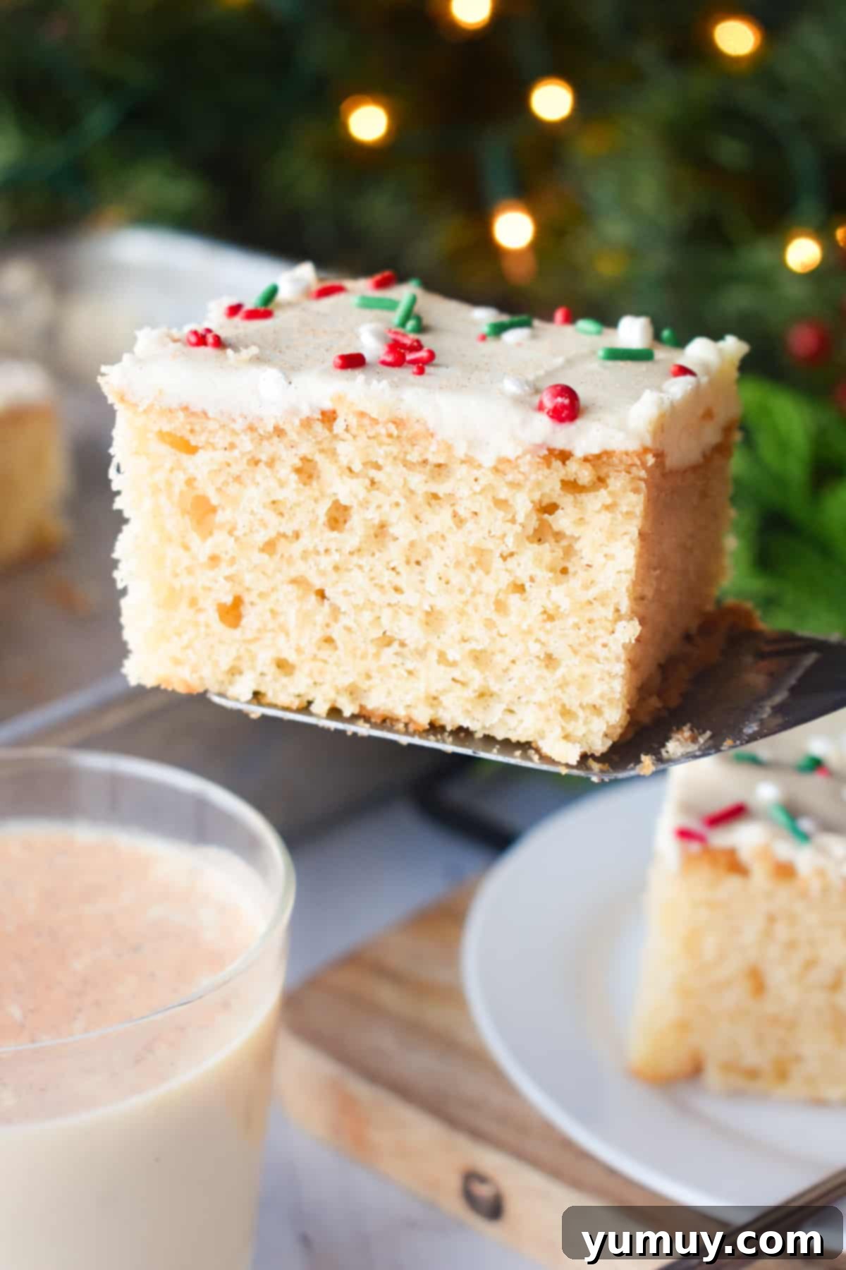 A perfectly portioned slice of moist eggnog sheet cake, showcasing the fluffy frosting and festive appearance, carefully lifted by a spatula.