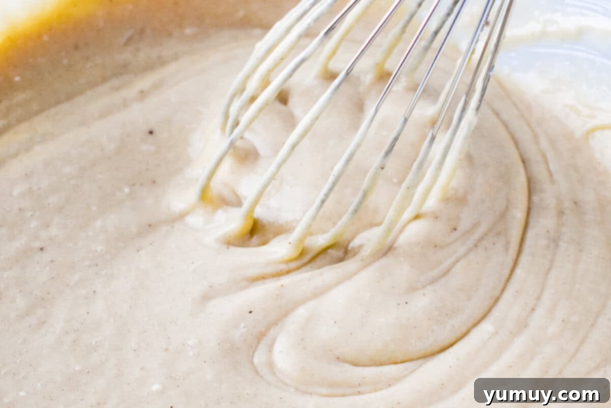 A smooth, creamy eggnog sheet cake batter resting in a clear glass bowl, with a whisk nearby, ready for baking.