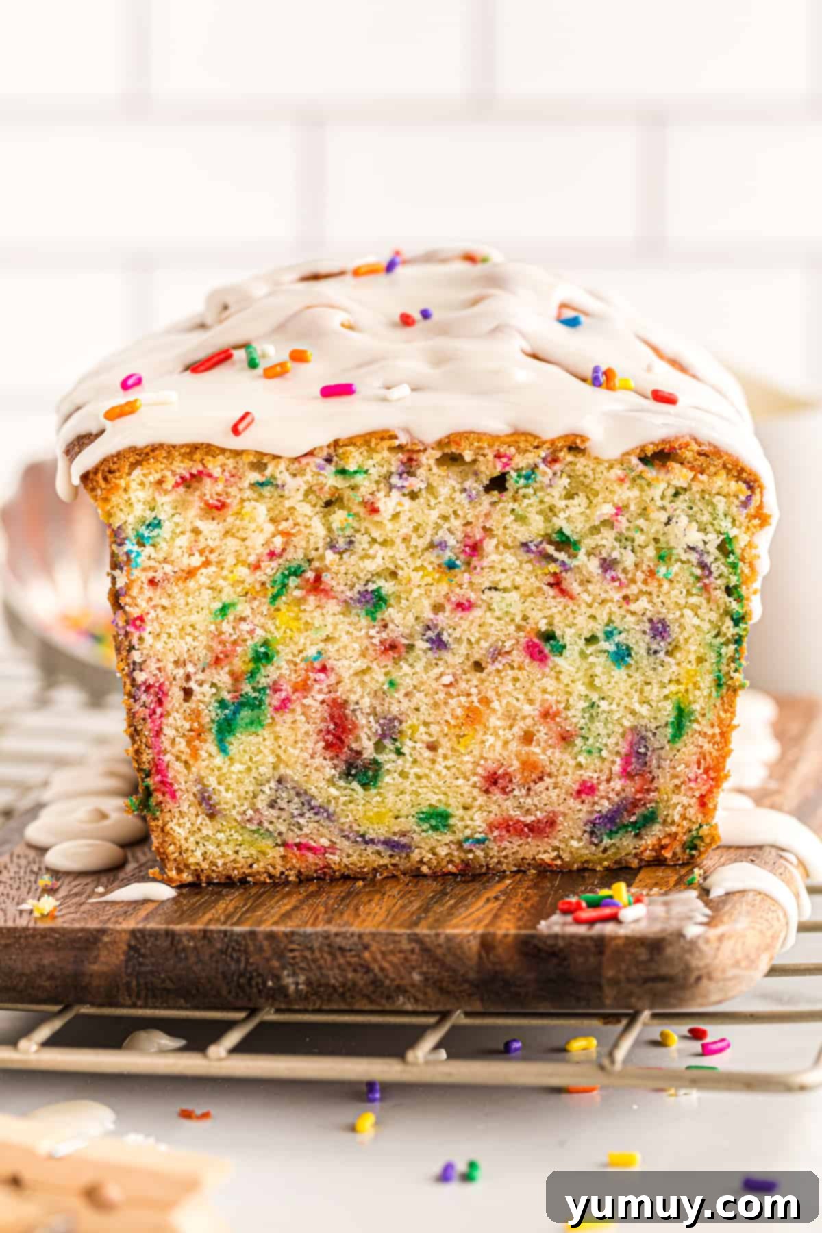 A slice of funfetti pound cake with glaze drizzled on top, showing the vibrant inside texture with rainbow sprinkles.