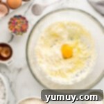 Eggs being added one by one to the wet ingredients in a glass bowl.