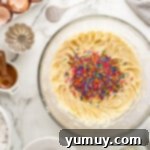 Rainbow sprinkles being folded into the pound cake batter in a glass bowl.