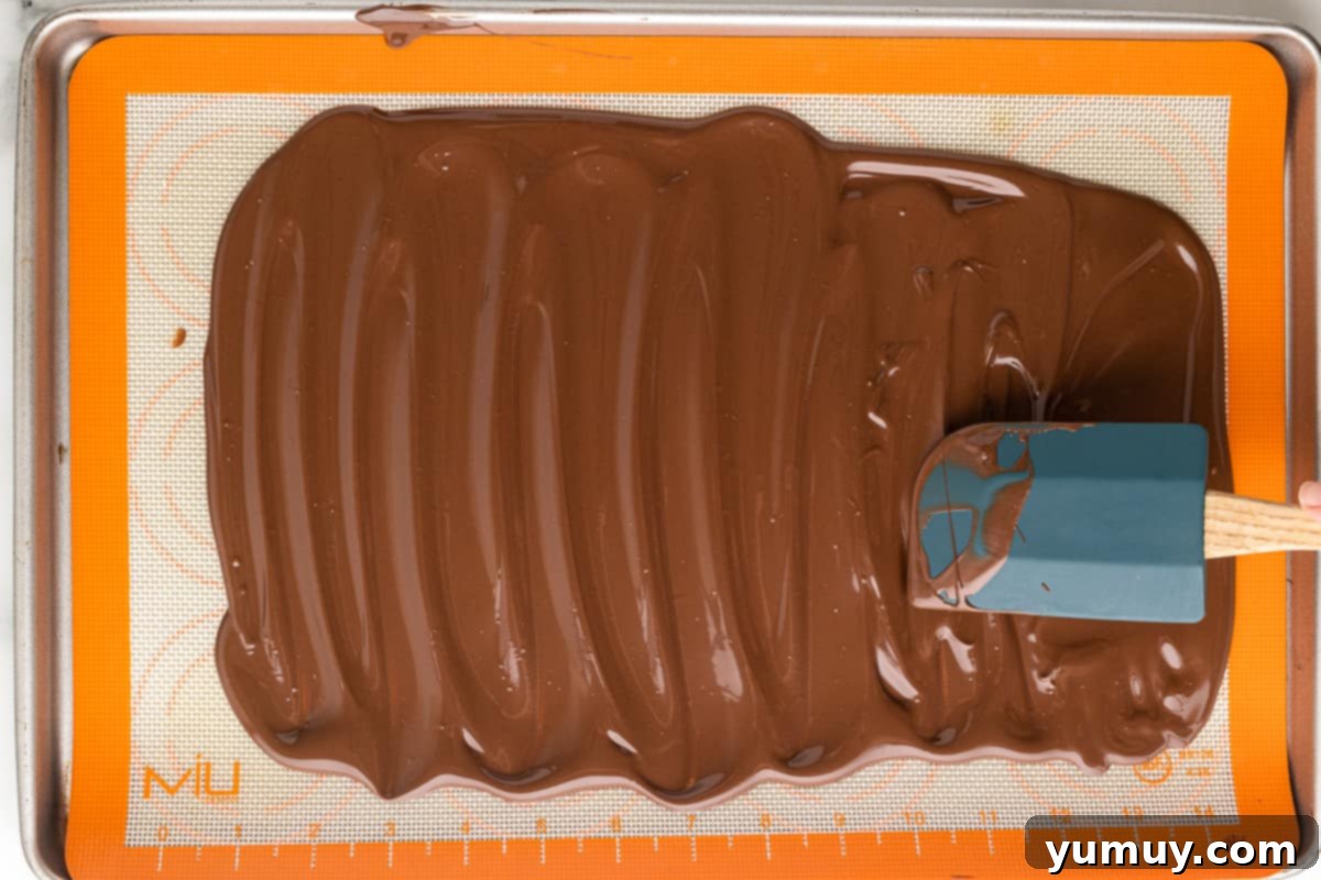 Spreading melted chocolate onto a baking tray lined with a silicone mat.