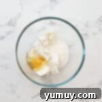 cream cheese, sugar, and an egg in a glass bowl.