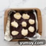 dollops of sweetened cream cheese over brownie batter in a foil-lined baking pan.