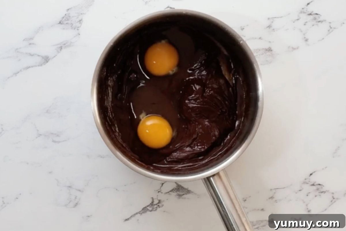 adding two eggs to melted chocolate and butter in a saucepan.