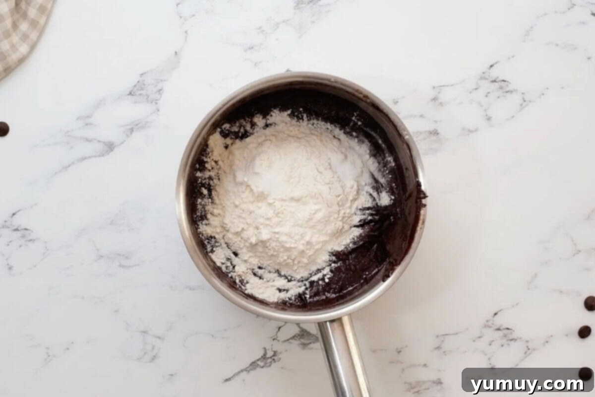 adding flour, baking soda, and salt to wet ingredients for brownies in a saucepan.