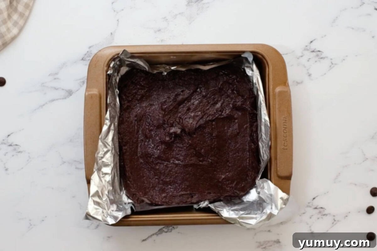 brownie batter spread out in a foil-lined baking pan.